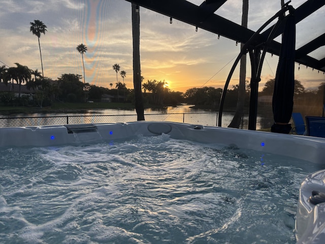 pool at dusk featuring a water view and a hot tub