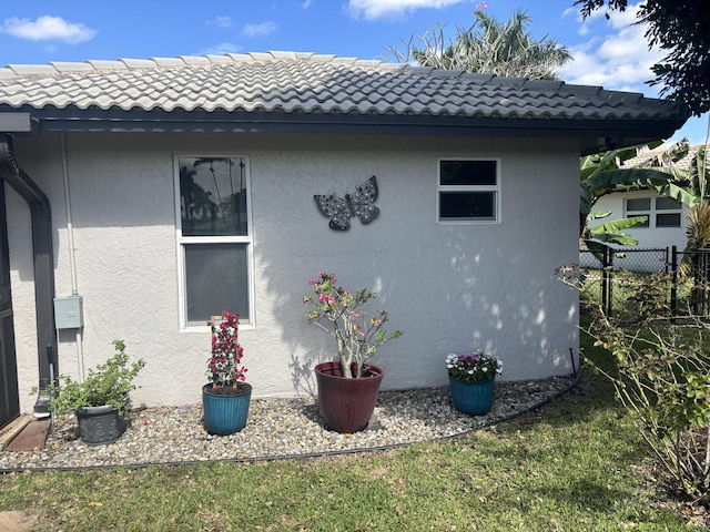 view of property exterior featuring stucco siding, a tile roof, and fence