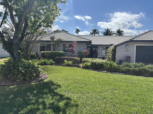 ranch-style home with a front yard, an attached garage, a tile roof, and stucco siding