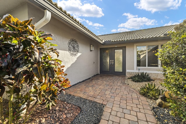 property entrance featuring a tile roof, french doors, and stucco siding