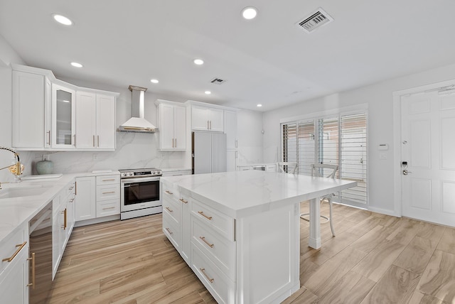 kitchen featuring visible vents, a sink, a center island, stainless steel appliances, and wall chimney range hood