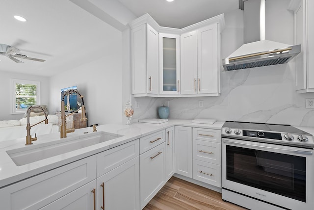 kitchen with stainless steel electric stove, a sink, decorative backsplash, white cabinetry, and wall chimney exhaust hood