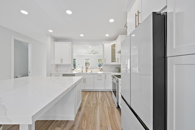 kitchen featuring fridge, stainless steel electric range oven, white cabinetry, and a sink