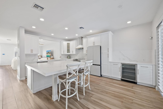 kitchen featuring beverage cooler, visible vents, white cabinets, fridge, and wall chimney range hood