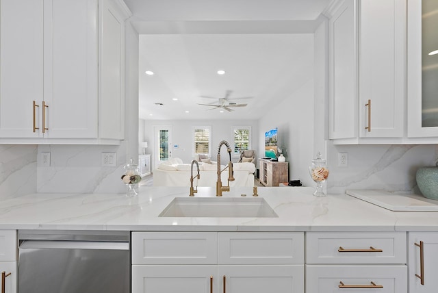 kitchen featuring light stone counters, a sink, white cabinets, stainless steel dishwasher, and backsplash