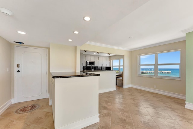 kitchen with dark countertops, stainless steel microwave, a peninsula, and baseboards