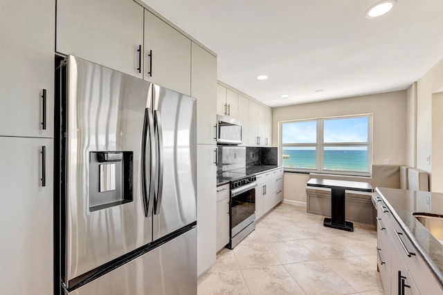 kitchen with a water view, backsplash, recessed lighting, dark stone counters, and appliances with stainless steel finishes