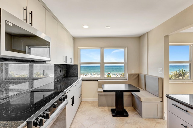 kitchen featuring dark stone countertops, range with electric cooktop, stainless steel microwave, tasteful backsplash, and breakfast area