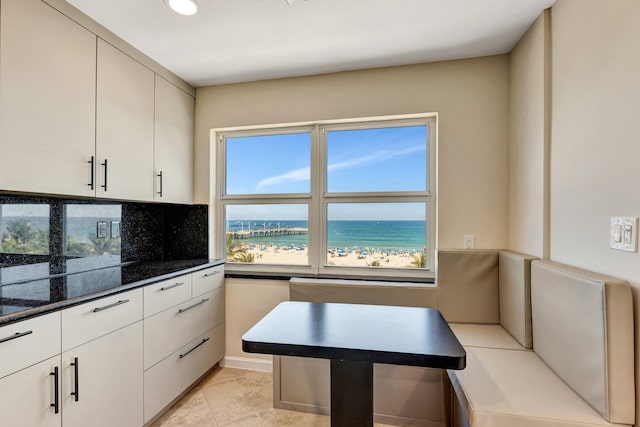 kitchen featuring decorative backsplash, a beach view, white cabinets, and a water view