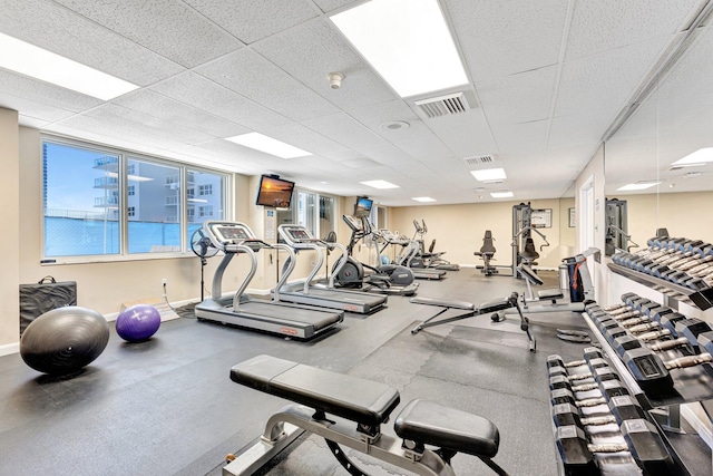 exercise room featuring visible vents, a paneled ceiling, and baseboards