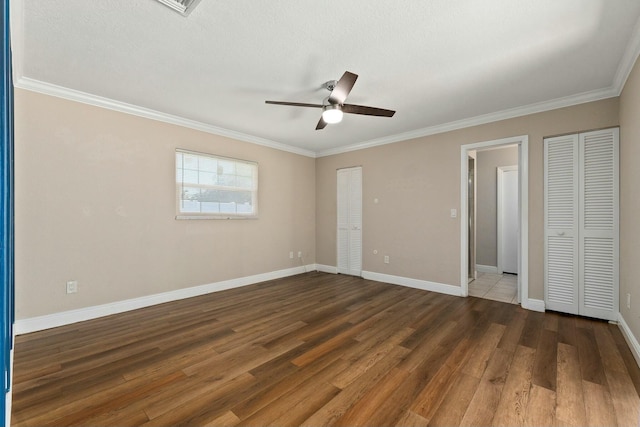 unfurnished bedroom with baseboards, dark wood-type flooring, ornamental molding, and a ceiling fan