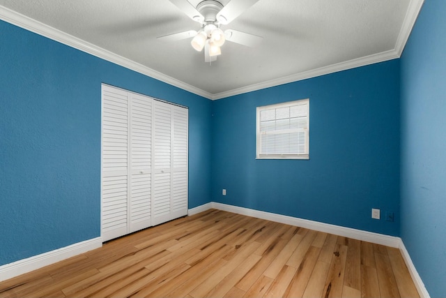 unfurnished bedroom featuring crown molding, wood finished floors, baseboards, and a closet