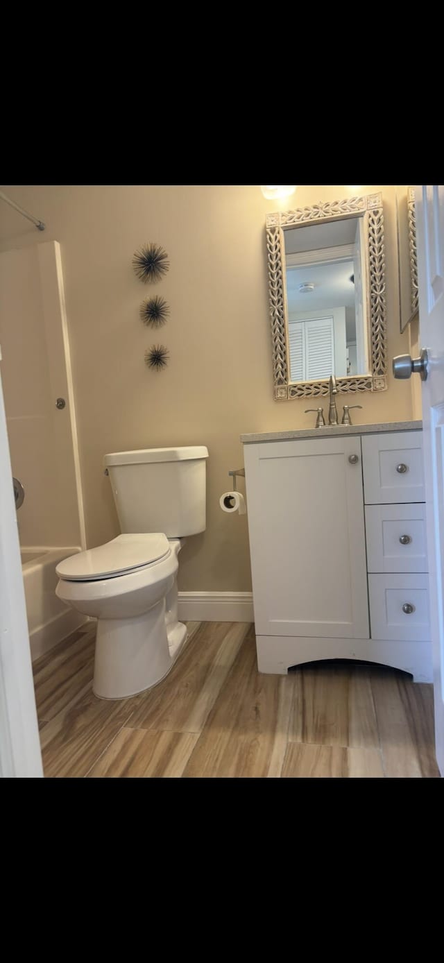bathroom with baseboards, toilet, wood finished floors, vanity, and  shower combination