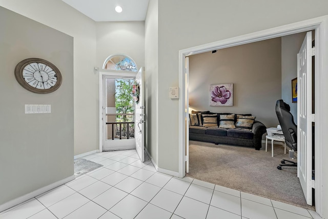 foyer featuring light tile patterned flooring, baseboards, a towering ceiling, and light carpet