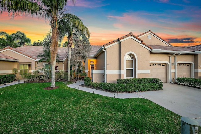 mediterranean / spanish home with stucco siding, a tiled roof, a yard, driveway, and an attached garage
