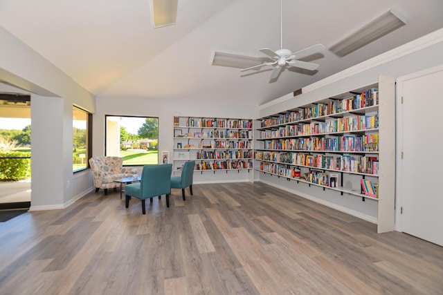 living area featuring built in shelves, wood finished floors, baseboards, lofted ceiling, and bookshelves