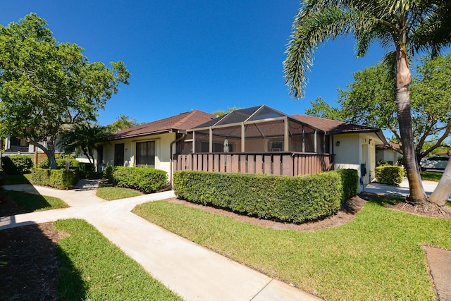 view of front of property featuring glass enclosure, a front lawn, and stucco siding