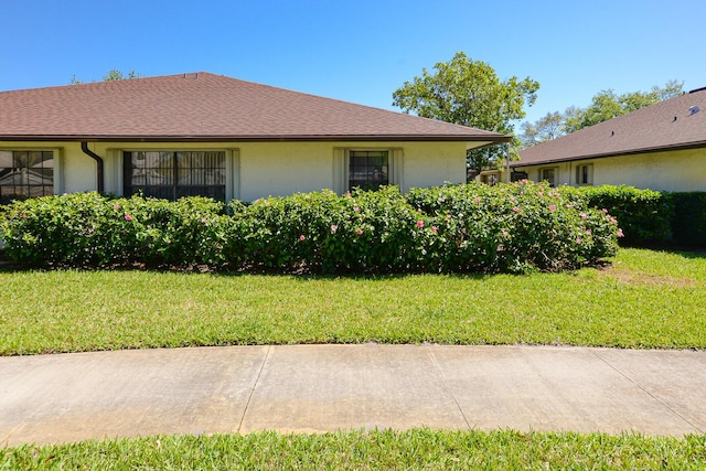 view of side of property featuring stucco siding, a lawn, and a shingled roof