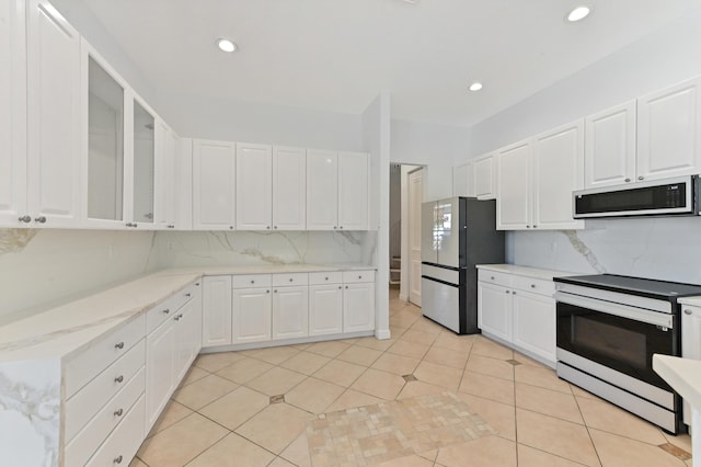 kitchen featuring light tile patterned floors, freestanding refrigerator, electric range oven, white cabinets, and backsplash