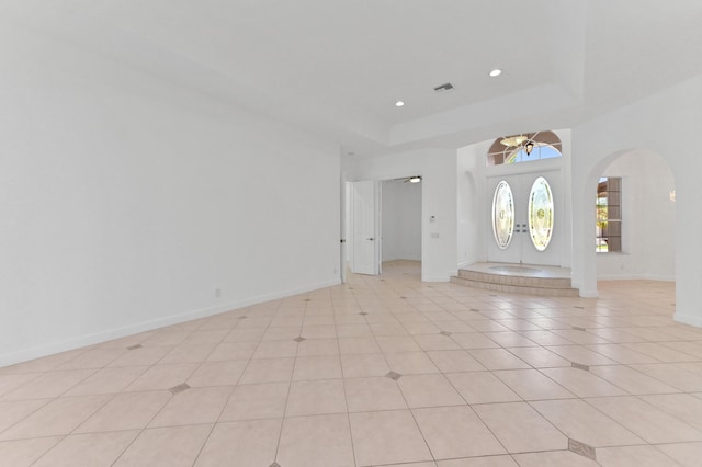 foyer entrance with light tile patterned floors, baseboards, recessed lighting, arched walkways, and a raised ceiling