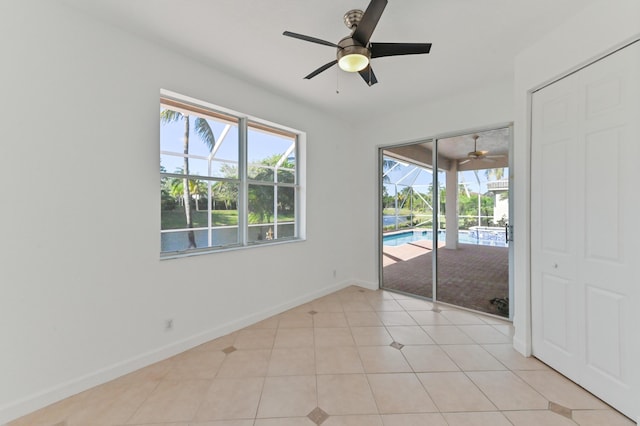 empty room with light tile patterned floors, a ceiling fan, baseboards, and a sunroom