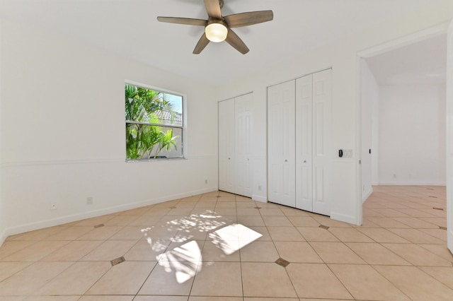 unfurnished bedroom with light tile patterned floors, baseboards, multiple closets, and ceiling fan