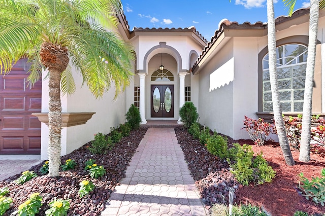 property entrance with a tiled roof, french doors, a garage, and stucco siding