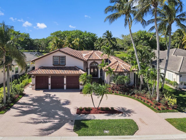 mediterranean / spanish house featuring a tiled roof, decorative driveway, a garage, and stucco siding