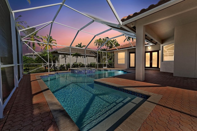 pool at dusk featuring glass enclosure, french doors, a pool with connected hot tub, and a patio