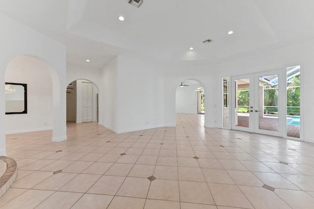 unfurnished room with a tray ceiling, french doors, and arched walkways