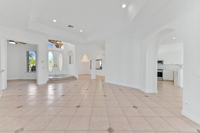 entryway with visible vents, a tray ceiling, recessed lighting, light tile patterned flooring, and arched walkways