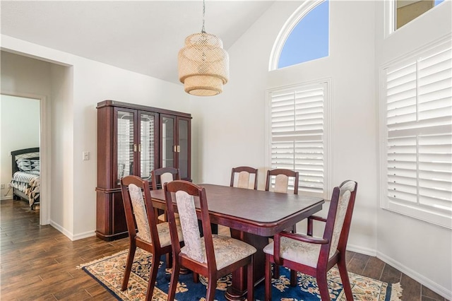 dining area featuring dark wood finished floors, baseboards, and high vaulted ceiling