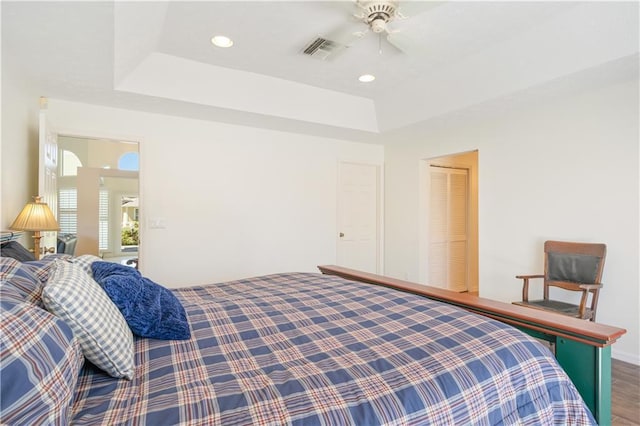 bedroom with a tray ceiling, visible vents, wood finished floors, and recessed lighting