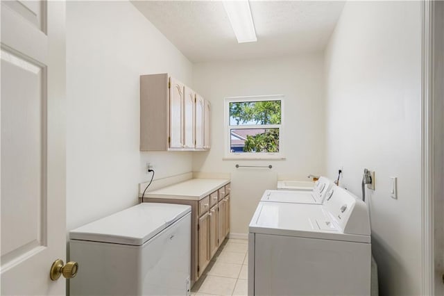 laundry room with a textured ceiling, light tile patterned floors, cabinet space, and washing machine and clothes dryer