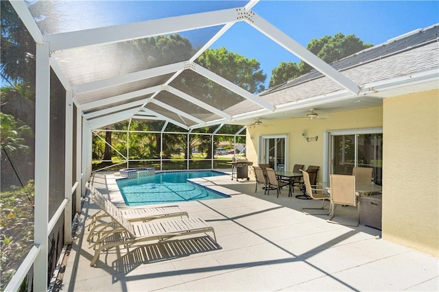 view of pool featuring glass enclosure, a patio, outdoor dining space, a ceiling fan, and a pool with connected hot tub