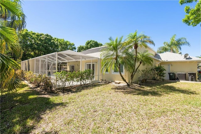 back of property with a lanai, central AC, stucco siding, a yard, and an attached garage