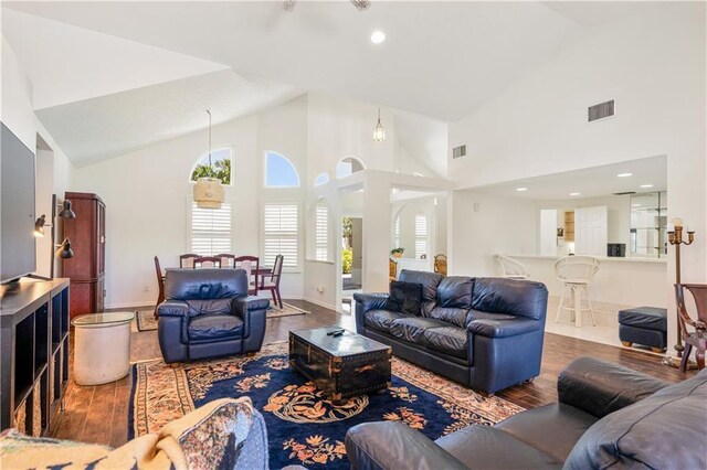 living area with visible vents, high vaulted ceiling, baseboards, and wood finished floors