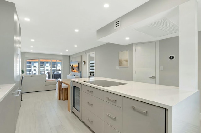 kitchen featuring wine cooler, black electric stovetop, open floor plan, and light countertops