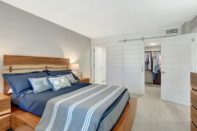 bedroom with a spacious closet, a closet, light wood-style floors, and a barn door