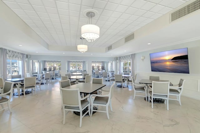 dining area featuring a decorative wall, visible vents, wainscoting, and a raised ceiling