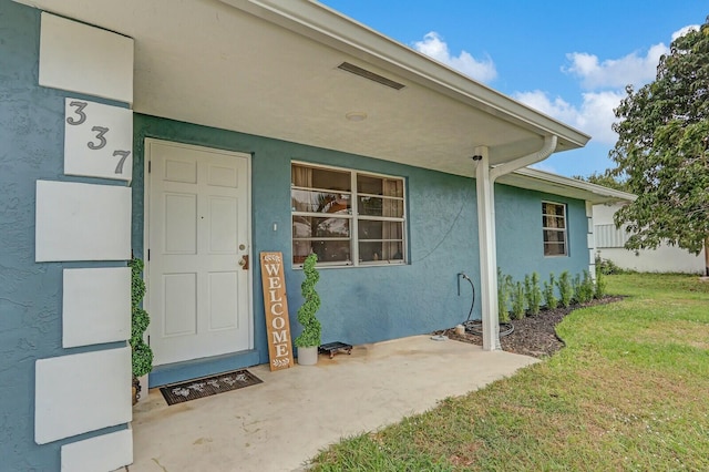 view of exterior entry with a yard and stucco siding