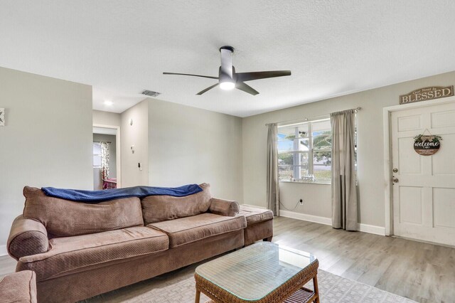 living area featuring a ceiling fan, baseboards, visible vents, a textured ceiling, and light wood-type flooring