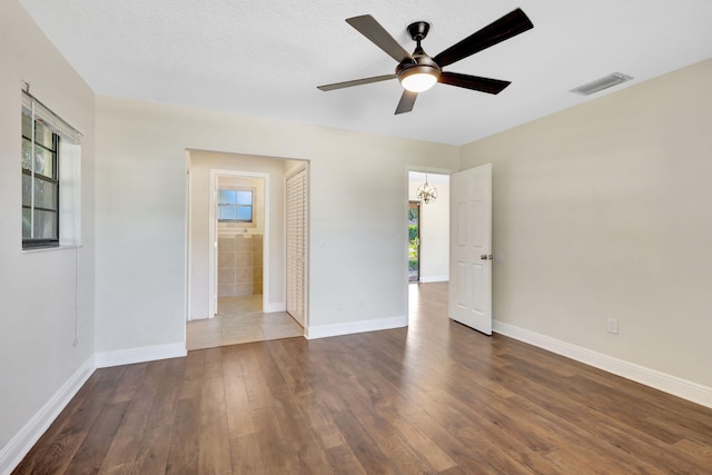 spare room with visible vents, ceiling fan with notable chandelier, a textured ceiling, wood finished floors, and baseboards