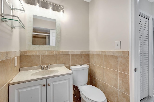 full bath featuring a wainscoted wall, toilet, vanity, tiled shower, and tile walls