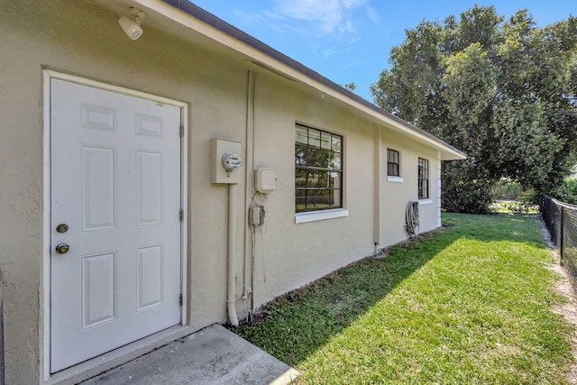 entrance to property with stucco siding, a yard, and fence