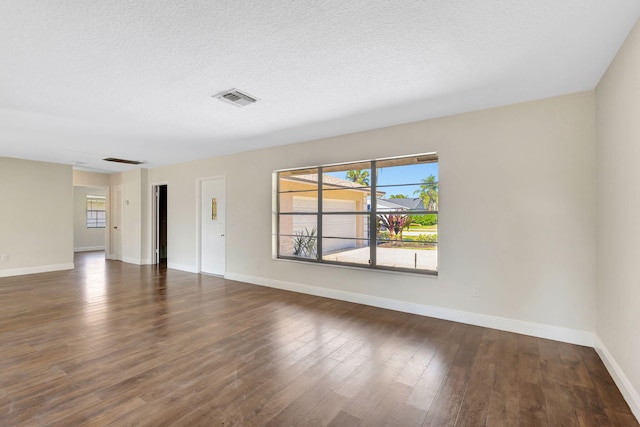 spare room featuring dark wood finished floors, baseboards, visible vents, and a textured ceiling