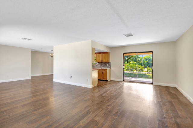 unfurnished living room with an inviting chandelier, dark wood-style floors, visible vents, and baseboards