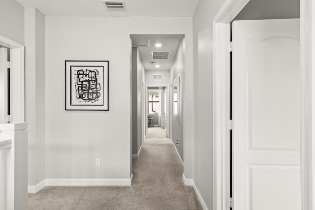 hallway featuring visible vents, carpet floors, and baseboards