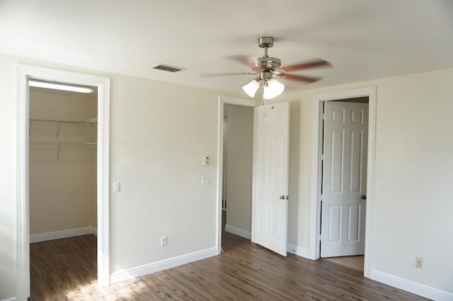 unfurnished bedroom with a spacious closet, visible vents, baseboards, and wood finished floors