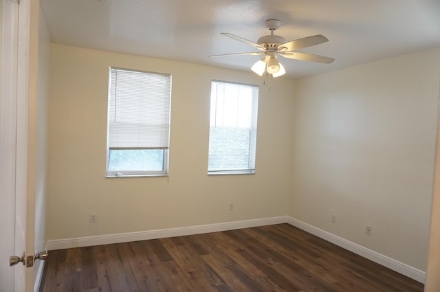 empty room featuring a wealth of natural light, baseboards, dark wood-type flooring, and ceiling fan